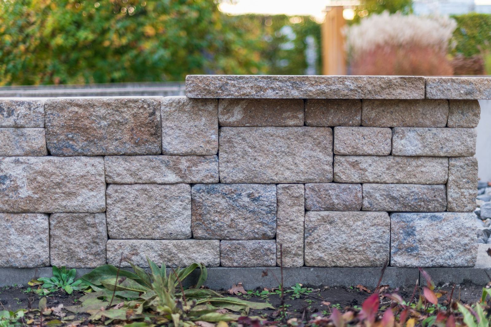 A stacked stone block retaining wall along a garden bed